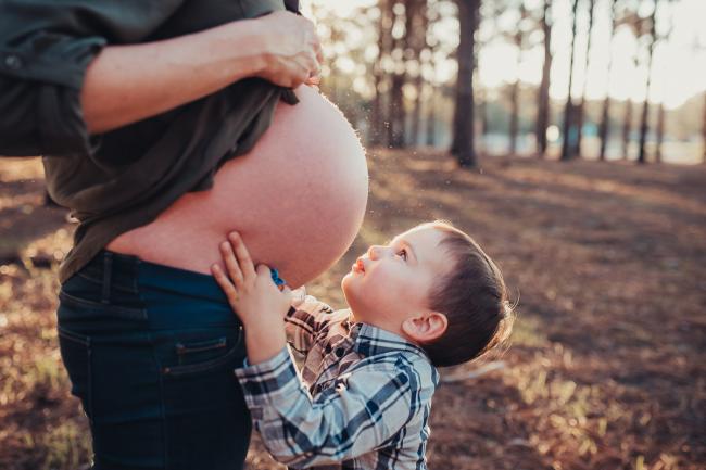 Little boy reaching to kiss his mother's pregnant bare tummy during a Perth maternity photography session at The Pines at golden hour