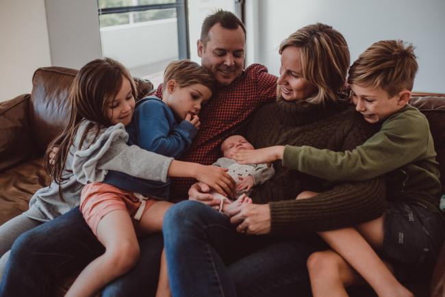 Newborn-Lifestyle-Photographer-Perth-12-of-54 Siblings reaching over to touch their new baby sister who is sitting on their mother's lap during a lifestyle newborn photography session in Perth