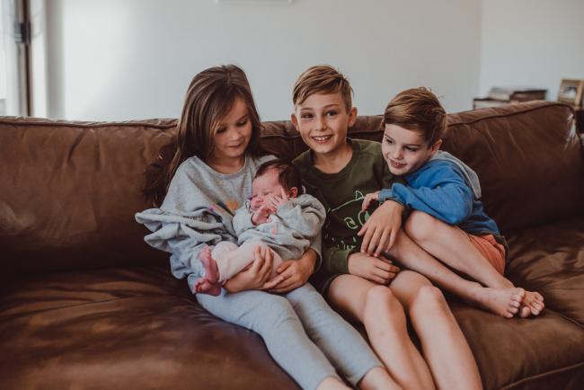 Newborn-Lifestyle-Photographer-Perth-17-of-54 Little girl holding her new baby sister with her brothers next to her during a lifestyle newborn photography session in Perth
