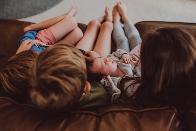 Top down image of new baby sister laying on the laps of her siblings during a Newborn Lifestyle photography session in Perth