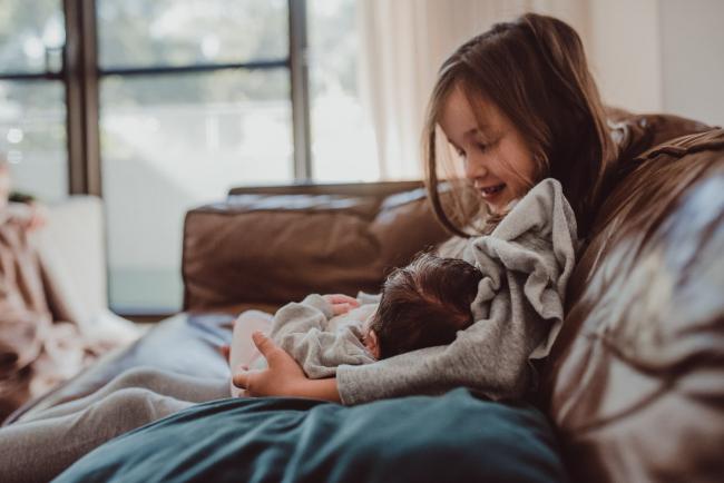 Newborn-Lifestyle-Photographer-Perth-22-of-54 Side on image of little girl holding her new baby sister during a lifestyle newborn photography session in Perth