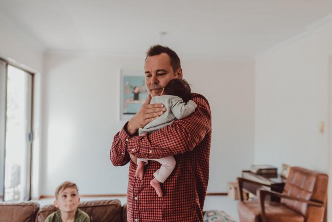 Newborn-Lifestyle-Photographer-Perth-23-of-54 Father holding his new baby as his son looks up at them during a lifestyle newborn photography session in Perth