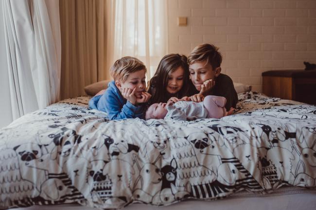 Newborn-Lifestyle-Photographer-Perth-34-of-54 Three siblings looking at their baby sister who is laying in front of them during a lifestyle newborn photography session in Perth