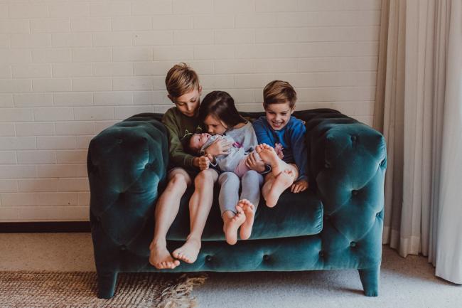 Newborn-Lifestyle-Photographer-Perth-36-of-54 Three siblings holding their baby sister on a green arm chair during a lifestyle newborn photography session in Perth
