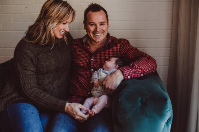 Newborn-Lifestyle-Photographer-Perth-37-of-54 Parents on a green arm chair holding their new baby during a lifestyle newborn photography session in Perth