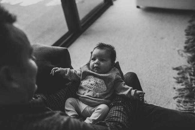 Newborn-Lifestyle-Photographer-Perth-40-of-54 Black and white image of baby laying on her father's lap during a lifestyle newborn photography session in Perth