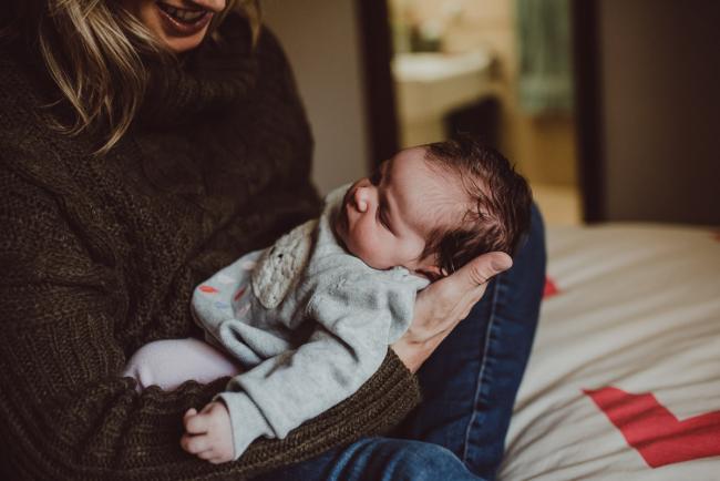 Mother holding her new baby out in front of her and smiling during a Newborn Lifestyle photography session in Perth