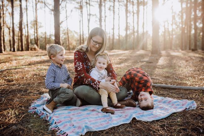 The-Pines-Family-Photographer-Perth-11-of-60 Mother sitting on a blanket with her daughter on her lap and her two boys next to her during a Perth Family Photography session during Golden Hour at The Pines