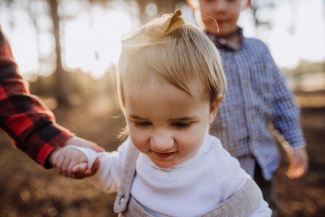 The-Pines-Family-Photographer-Perth-18-of-60 Close up of little girls face as her big brother holds her hand during a Perth Family Photography session during Golden Hour at The Pines