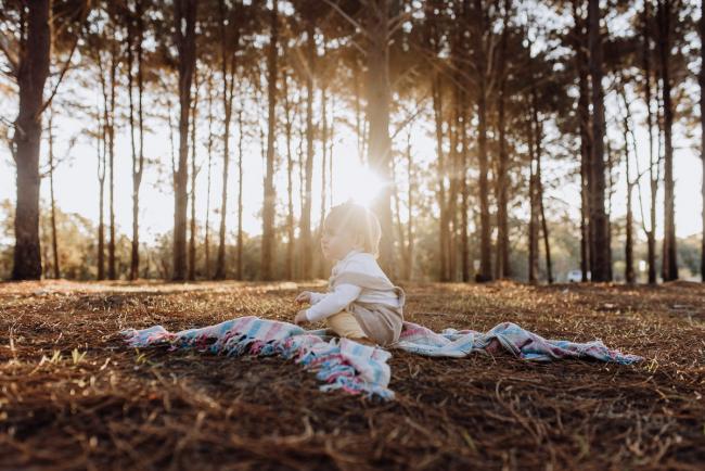 Little girl squatting on a blanket during a family photography Perth session at The Pines during golden hour