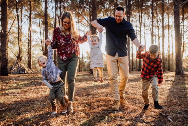 Mum and dad walking and lifting their 3 kids in the air during a family photography Perth session at The Pines during golden hour