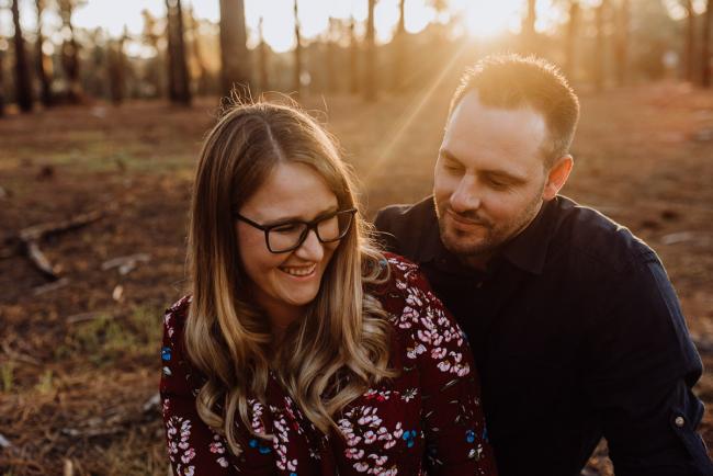 Couple sitting on the ground and wife laughing during a couple photography session in Perth during Golden hour at The Pines