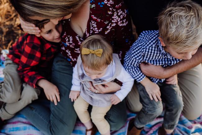 The-Pines-Family-Photographer-Perth-5-of-60 Top down image of three kids sitting on their parents laps during a Perth Family Photography session during Golden Hour at The Pines