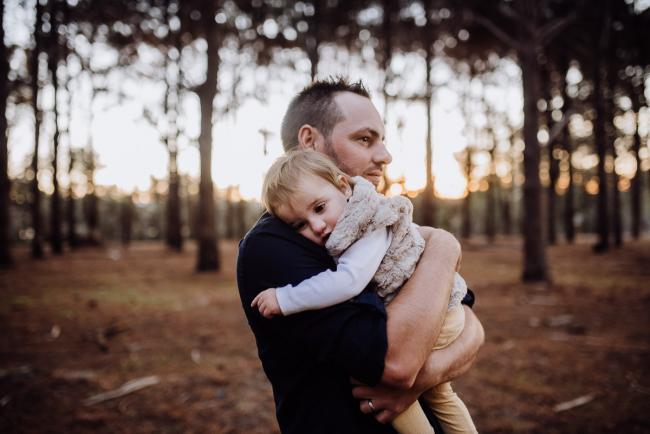 Little girl cuddling into her father during a family photography Perth session at The Pines during golden hour