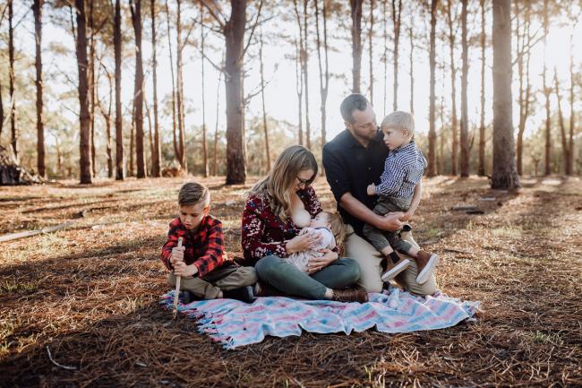 The-Pines-Family-Photographer-Perth-6-of-60 Father holding his son, mother breastfeeding her daughter, and their other son playing with a stick during a Perth Family Photography session during Golden Hour at The Pines