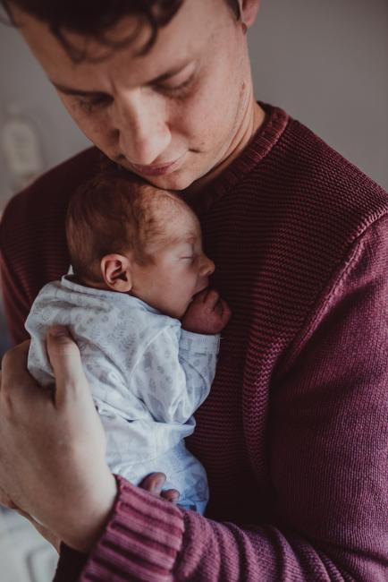 Father holding new baby to his chest during a Perth Fresh 48 photography session captured in home