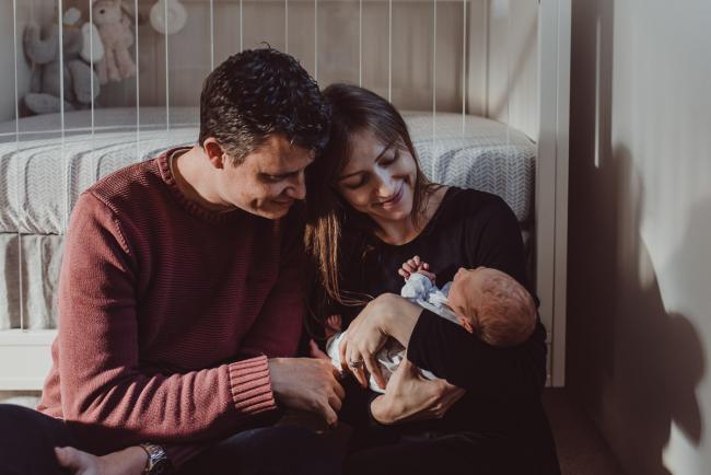New parents sitting against the cot and smiling at their new baby during a Perth Fresh 48 photography session captured in home