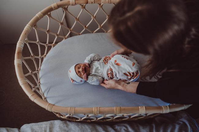 Top down image of mother reaching into wicker bassinet to pick up new baby with Perth lifestyle newborn photographer