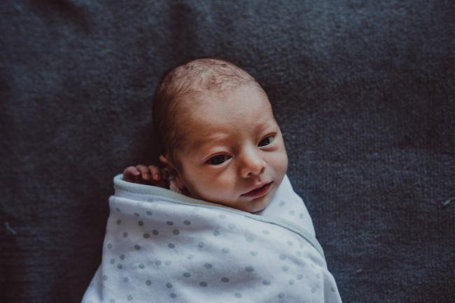 Wrapped baby with hand poking out with Perth lifestyle newborn photographer