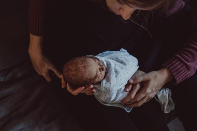 Mother holding baby in her hands as husband holds her hand during a Perth Fresh 48 photography session captured in home