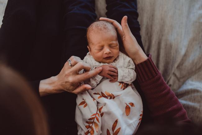 Parents touching new baby who is laying on their legs during a Perth Fresh 48 photography session captured in home