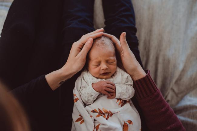 Parents touching the head of their new baby who is laying on their laps during a Perth Fresh 48 photography session captured in home