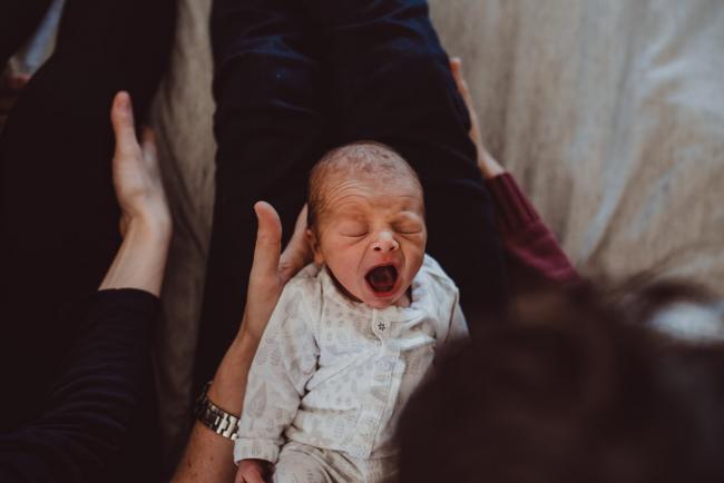 Baby yawning while laying on father's lap with Perth lifestyle newborn photographer