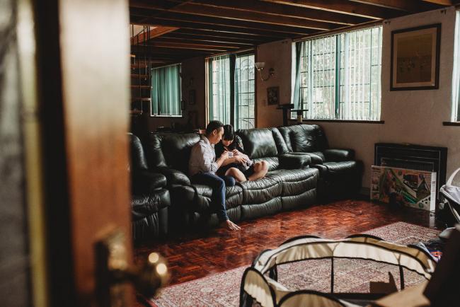 Looking through the doorway as parents sit on a green couch holding their new baby daughter during an in-home Perth Newborn Lifestyle photography session