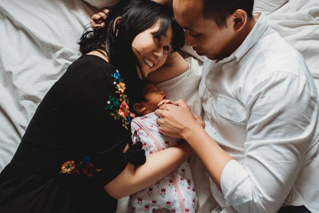 Parents laying on the bed cuddling their new baby daughter during an in-home Perth Newborn Lifestyle photography session