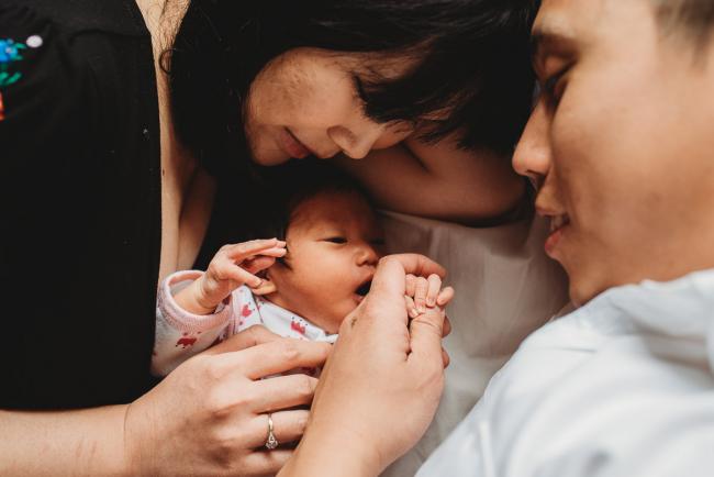 Close up of parents laying on the bed and cuddling their new baby daughter during an in-home Perth Newborn Lifestyle photography session