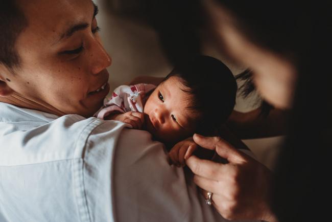 Parents looking at their new baby who is on her father's shoulder during an in-home Perth Newborn Lifestyle photography session