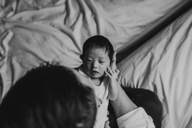 Black and white image of father holding new baby out to look at him during an in-home Perth Newborn Lifestyle photography session