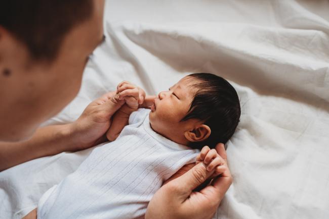 Father holding the hands of his new baby during an in-home Perth Newborn Lifestyle photography session