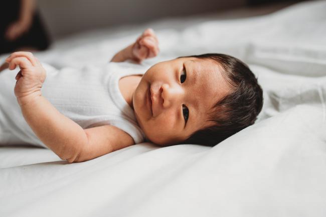 New baby laying on the bed and looking back at the camera during an in-home Perth Newborn Lifestyle photography session