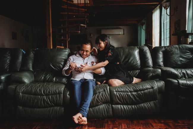 New parents sitting on a green couch holding their new baby daughter during an in-home Perth Newborn Lifestyle photography session