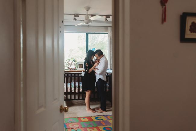 Looking through the doorway as parents hold their new baby in front of the cot during an in-home Perth Newborn Lifestyle photography session