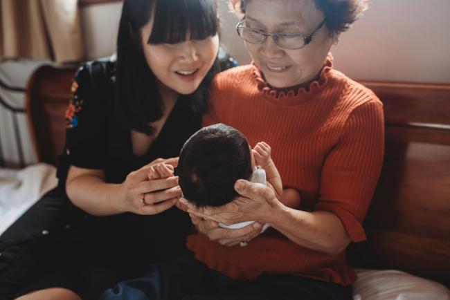 Mother and grandmother smile down at new baby during an in-home Perth Newborn Lifestyle photography session
