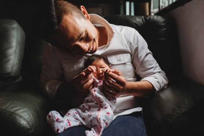 Father holding his new baby daughter and smiling during an in-home Perth Newborn Lifestyle photography session