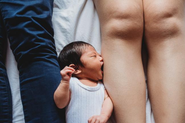 New baby laying between parents legs and sucking on her mother's leg during an in-home Perth Newborn Lifestyle photography session