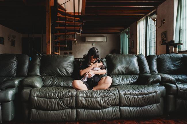 Mother sitting cross legged on a green couch holding her new baby daughter during an in-home Perth Newborn Lifestyle photography session