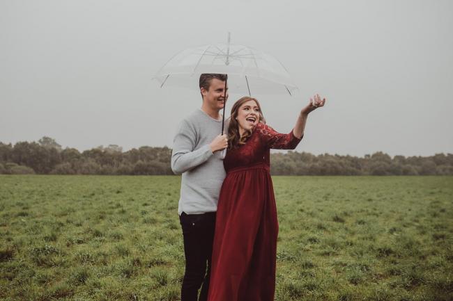Perth-Maternity-Photographer-Perrys-Paddock-13-of-39 Pregnant lady laughing as her hand is out in the rain as her and her partner stand under an umbrella during a Perth maternity session at Perry's Paddock during rain