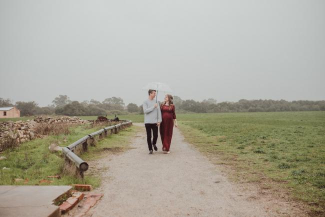 Pregnant couple walking down the path under an umbrella with Perth maternity photographer at Perry's Paddock