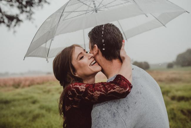 Perth-Maternity-Photographer-Perrys-Paddock-32-of-39 Woman laughing as she embraces her husband's head under an umbrella during a Perth maternity session at Perry's Paddock during rain
