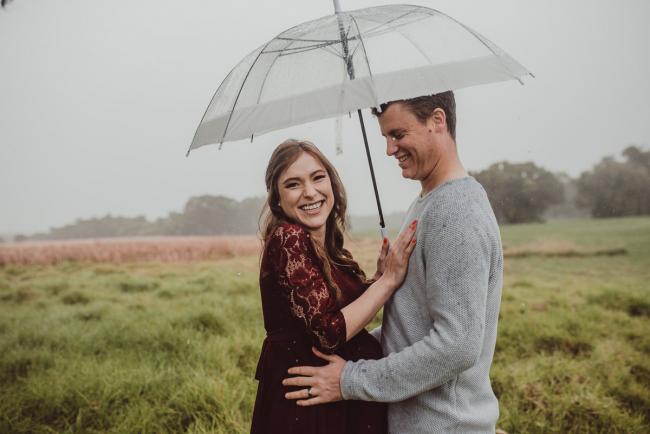 Pregnant couple laughing under an umbrella with Perth maternity photographer at Perry's Paddock