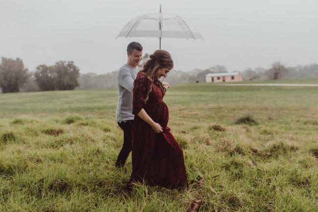 Pregnant couple walkign under an umbrella with Perth maternity photographer at Perry's Paddock