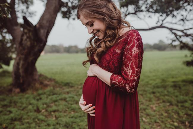 Perth-Maternity-Photographer-Perrys-Paddock-4-of-39 Lady in a red dress looking down at her baby bump during a Perth maternity session at Perry's Paddock during rain