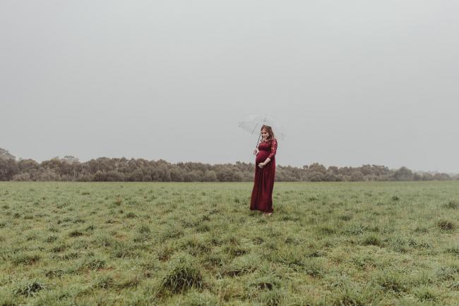 Perth-Maternity-Photographer-Perrys-Paddock-8-of-39 Lady in a red dress standing with an umbrella during a Perth maternity session at Perry's Paddock during rain