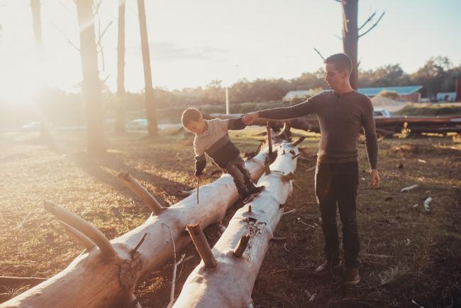 Father holding his son's hand who is balancing on a log with Perth family photographer at The Pines