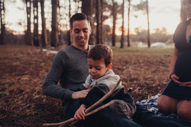 Perth-Maternity-Photographer-The-Pines-46-of-48 Boy playing with sticks on his dad's lap with Perth maternity photographer at The Pines