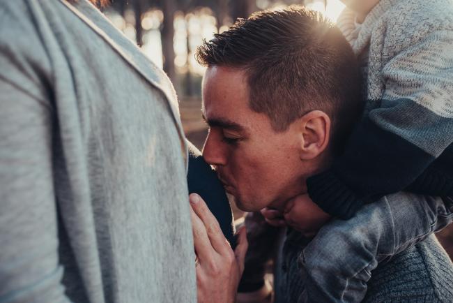 Husband kissing pregnant wife's tummy with son on his shoulders with Perth maternity photographer at The Pines